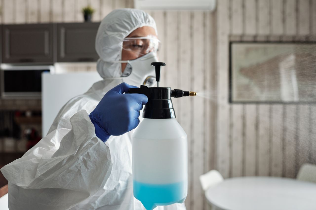 services-01 Professional in full gear disinfecting indoor area using a spray bottle for COVID-19 prevention.