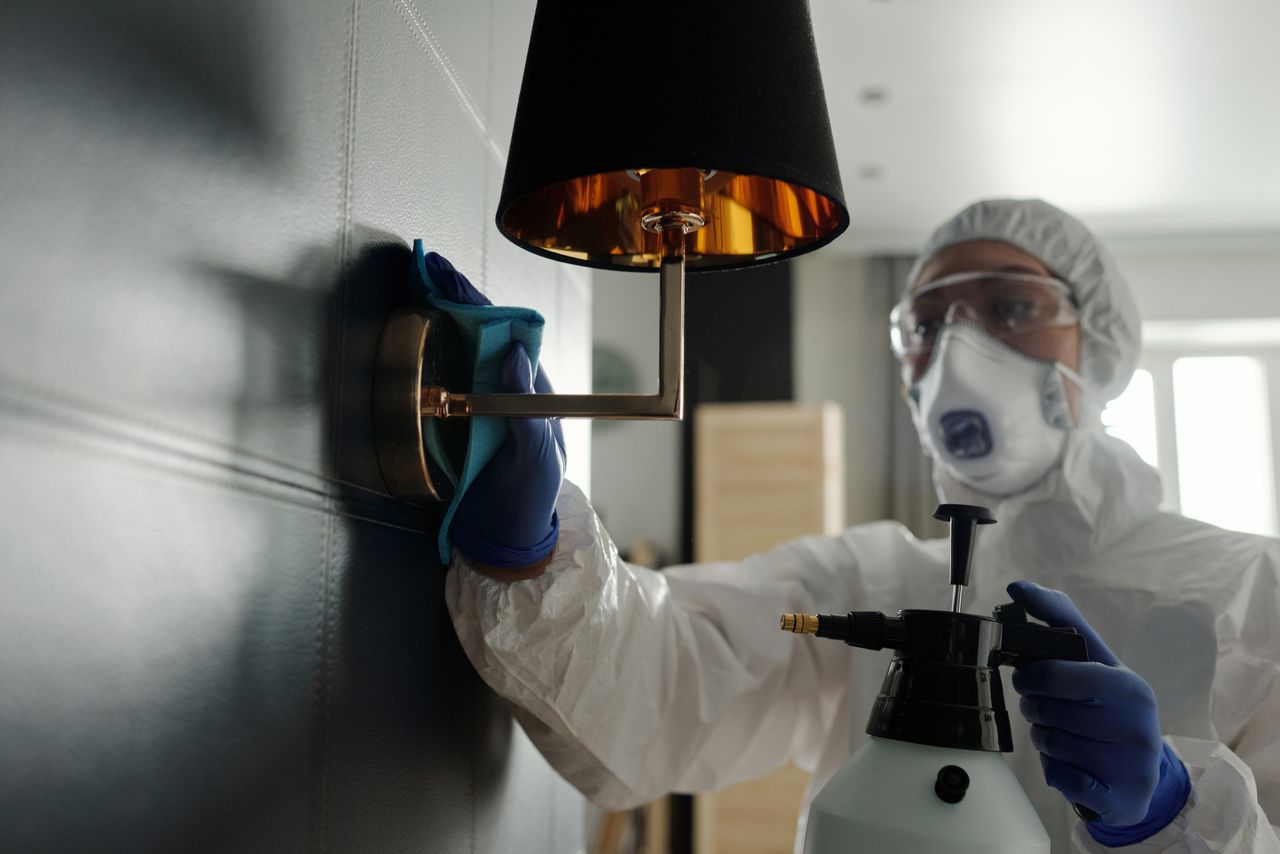why-choose-us A person wearing protective gear sanitizes a wall lamp to prevent virus spread.